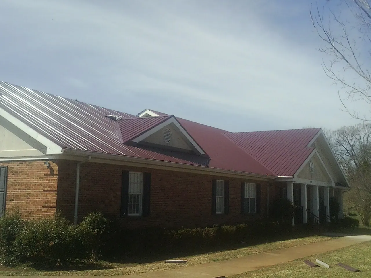 Red metal roof with gabled entries on a long brick building, from a Hail Damage Roof Repair job in Old Monroe