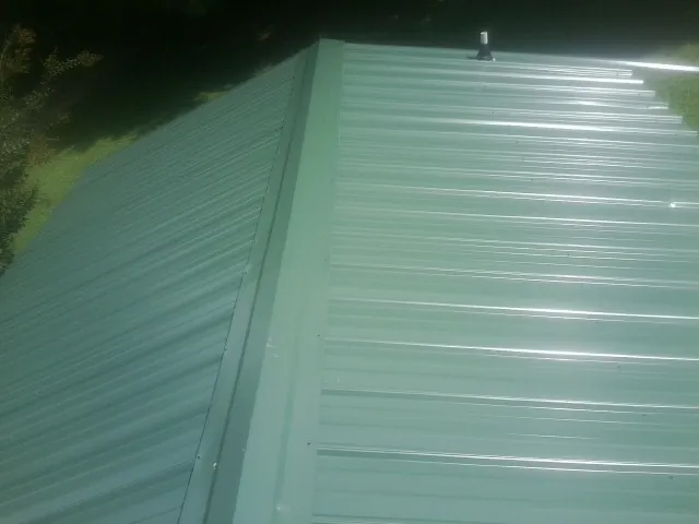 New green metal panels meeting at the ridge of a roof — Flat Roof Repair work by our crew in Old Monroe