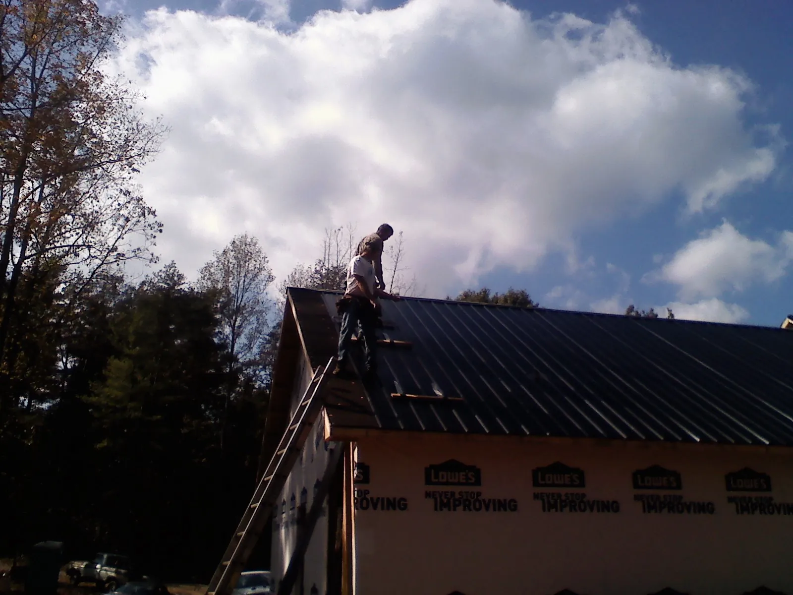 Roofer fastening dark metal panels high against a cloudy sky, from a Roof Inspection job in Old Monroe