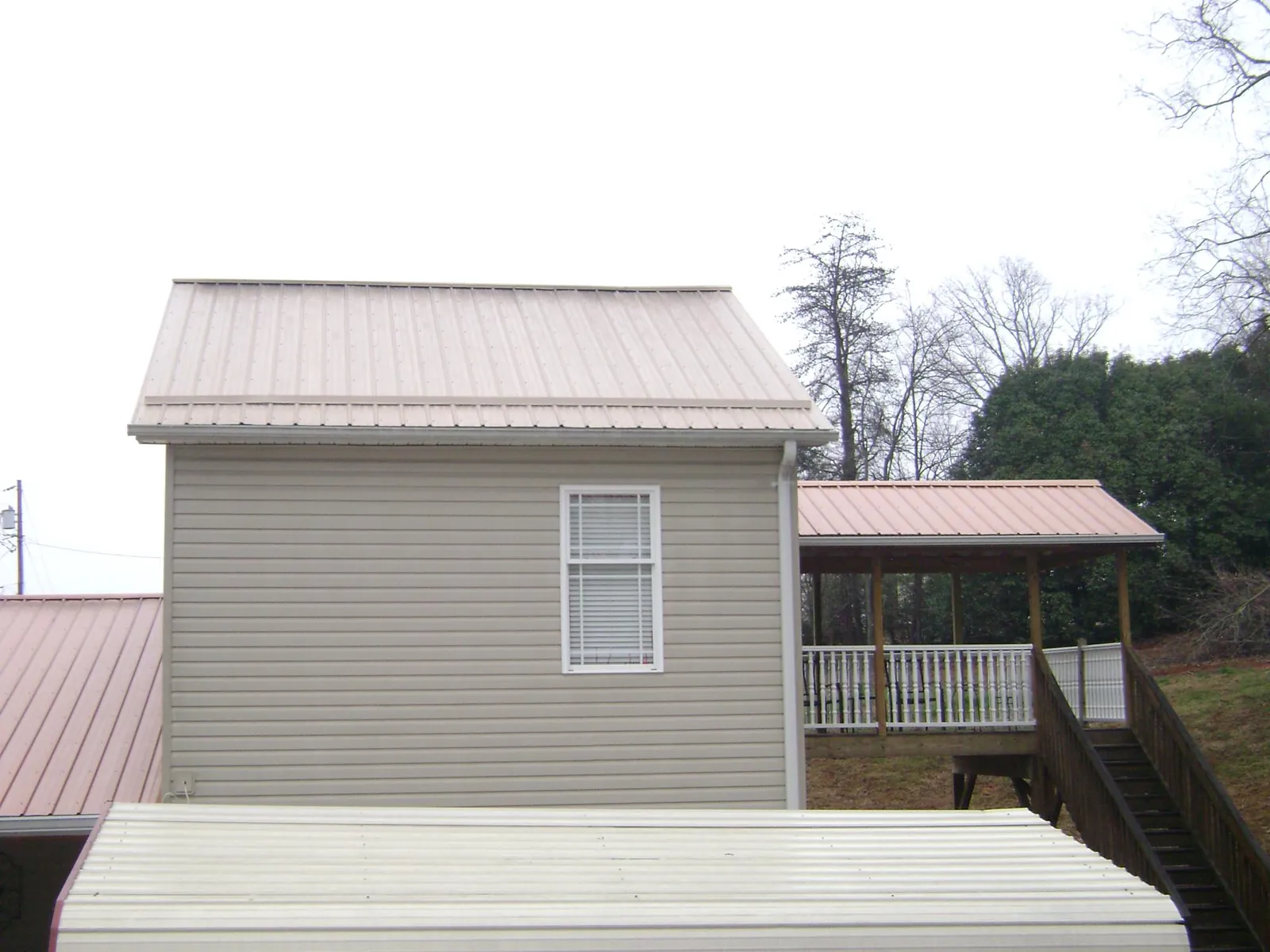 Tan metal roofs on a two story addition and attached porch, from a Roof Replacement job in Old Monroe